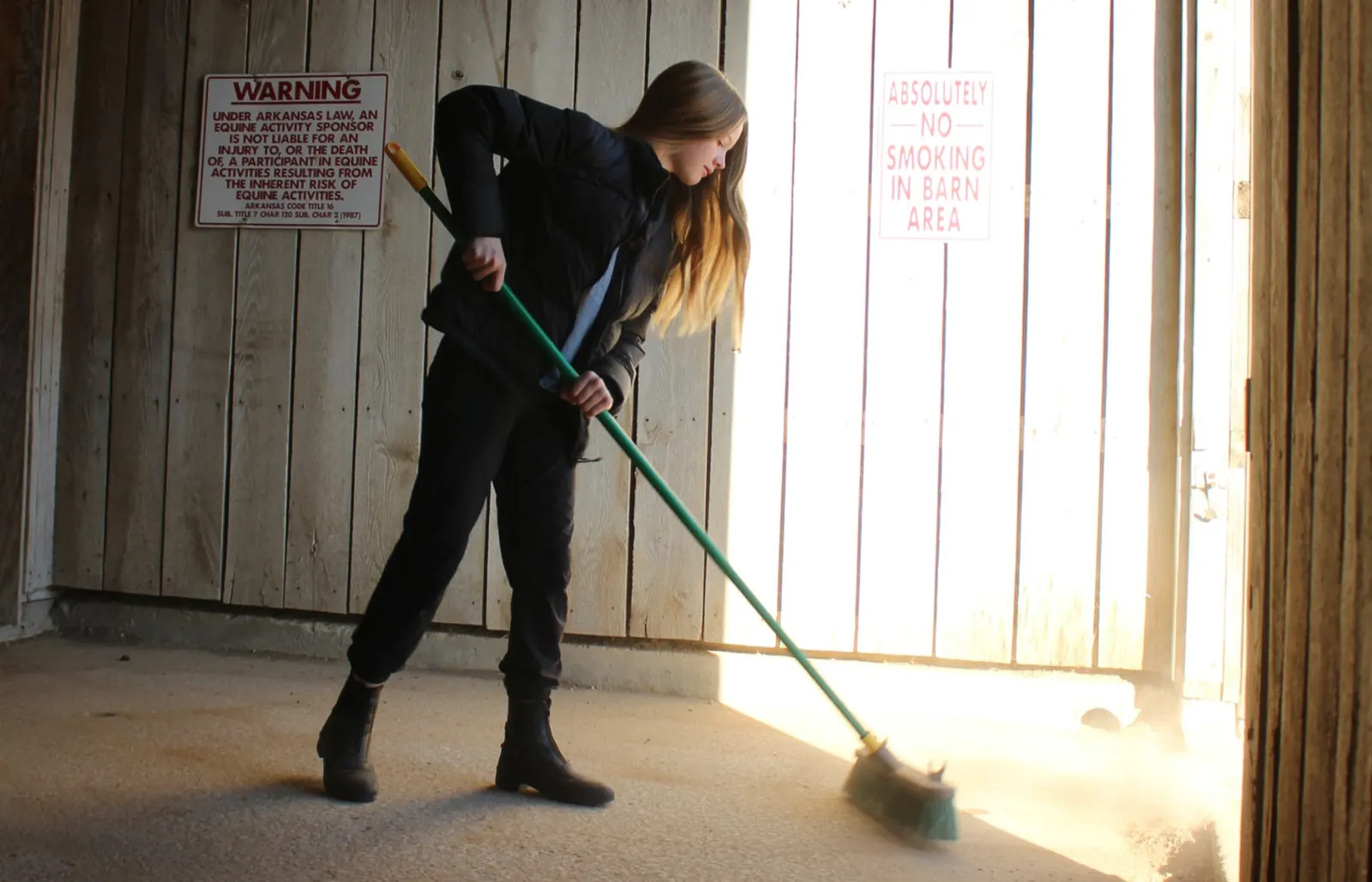 A volunteer sweeping the stable aisle
